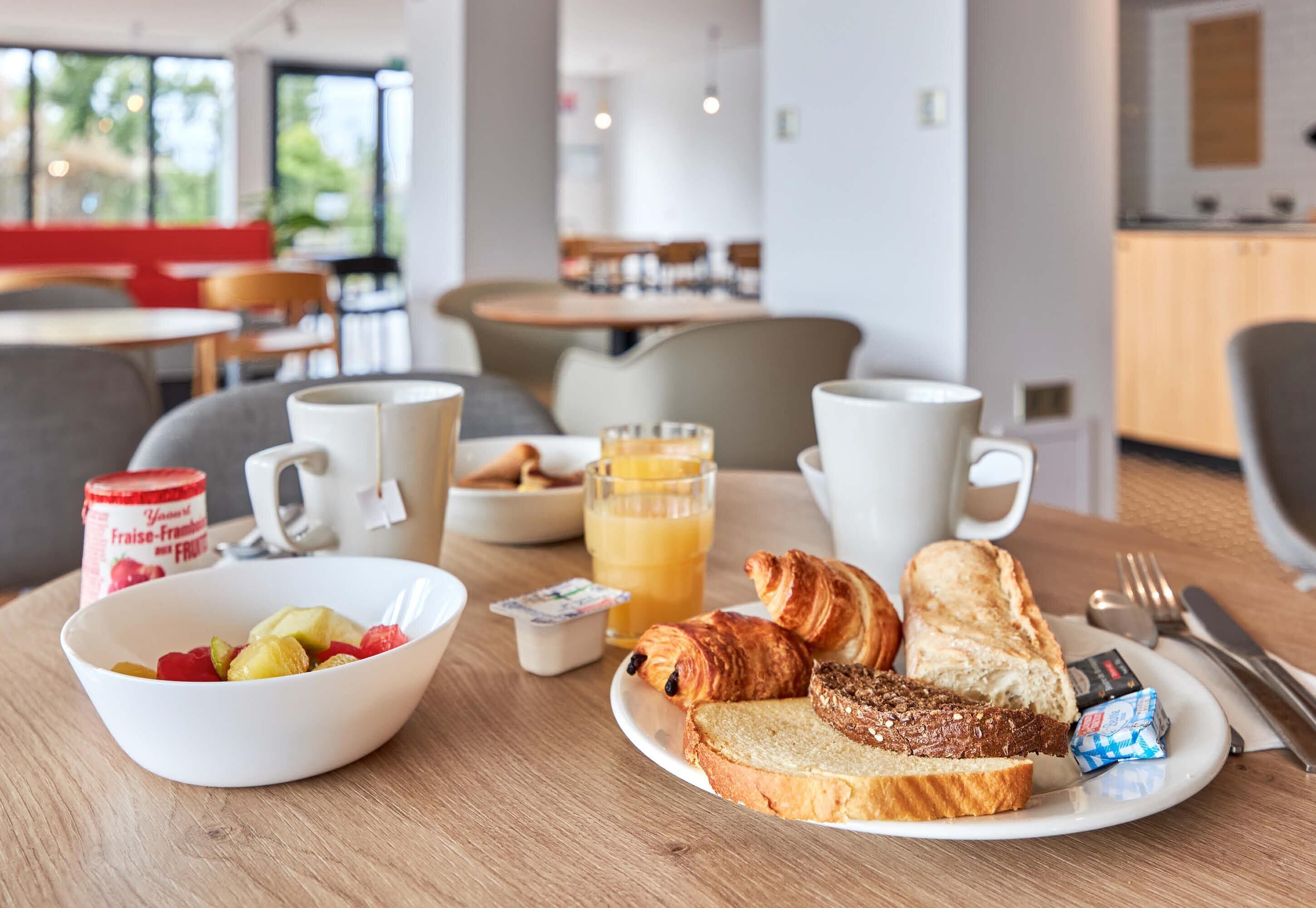 Ein Frühstückstisch mit einer Fruchtschale, Croissants, Toast und einem Glas Orangensaft.