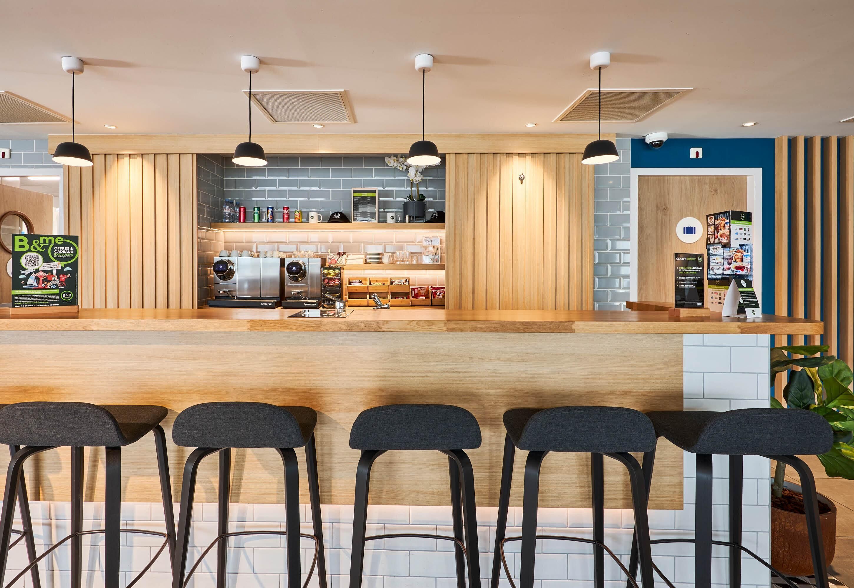 A modern bar area with a wooden counter, bar stools, pendant lighting, and a visible kitchen area with appliances.