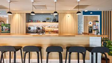Eine moderne Bar mit Holztresen, Barhocker, Pendelleuchten und einem sichtbaren Küchenbereich mit Geräten.