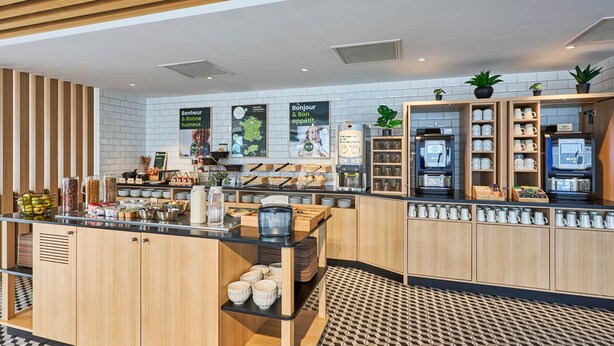 A modern cafe with wooden cabinetry, a coffee machine, and a variety of breakfast items on display. - B&B HOTEL Deauville-Touques (Touques)
