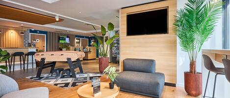 Un moderno vestíbulo de hotel con un mostrador de recepción de madera, asientos cómodos, una gran pantalla de televisión y plantas en macetas.