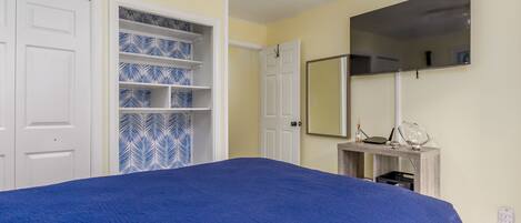 A bedroom with a bed, a wardrobe, a mirror, and a small table with a lamp.