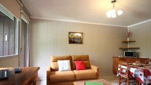 Una sala de estar con sofá, una mesita, un comedor con mesa y sillas, microondas y una lámpara en el techo.