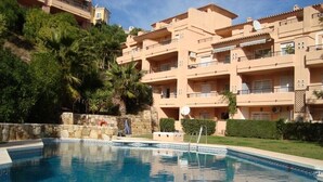 A swimming pool surrounded by a stone wall, with a building featuring balconies and a tiled roof in the background. - IDEAL FOR FAMILY HOLIDAYS (AN)