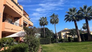 A building with balconies, a garden with palm trees, and a clear blue sky. - IDEAL FOR FAMILY HOLIDAYS (AN)
