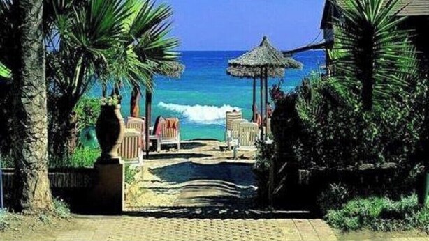 A beach view with a pathway leading to a seating area, palm trees, and a thatched structure. - IDEAL FOR FAMILY HOLIDAYS (AN)