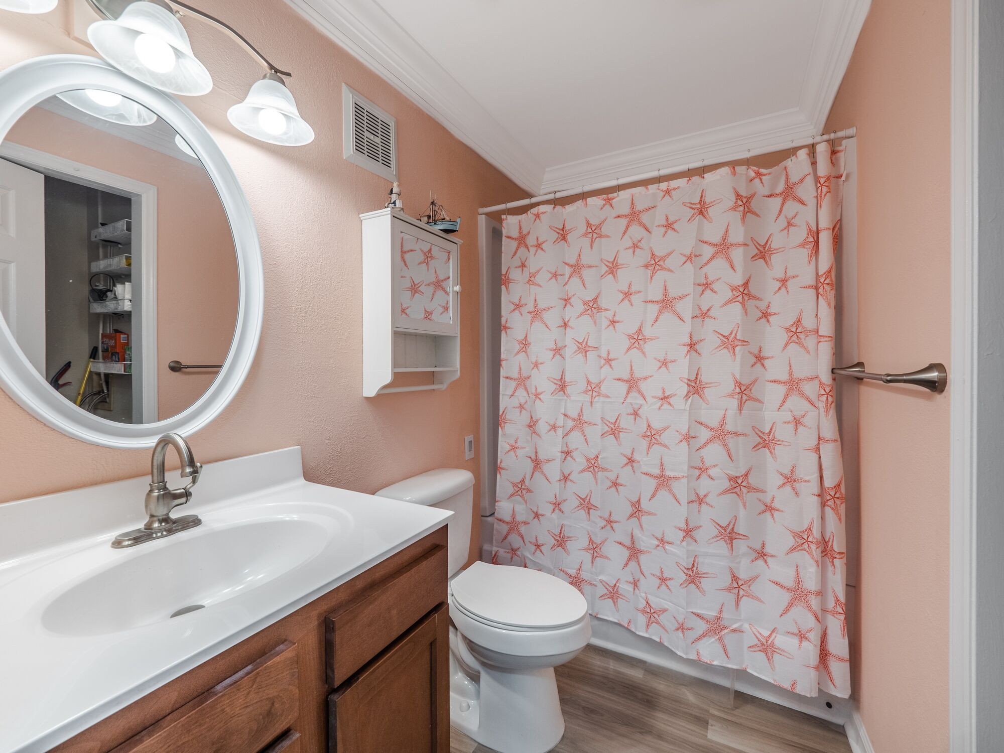 A bathroom with a white sink, wooden cabinet, and a toilet. There is a mirror with lights above it, and a shower curtain with star patterns.