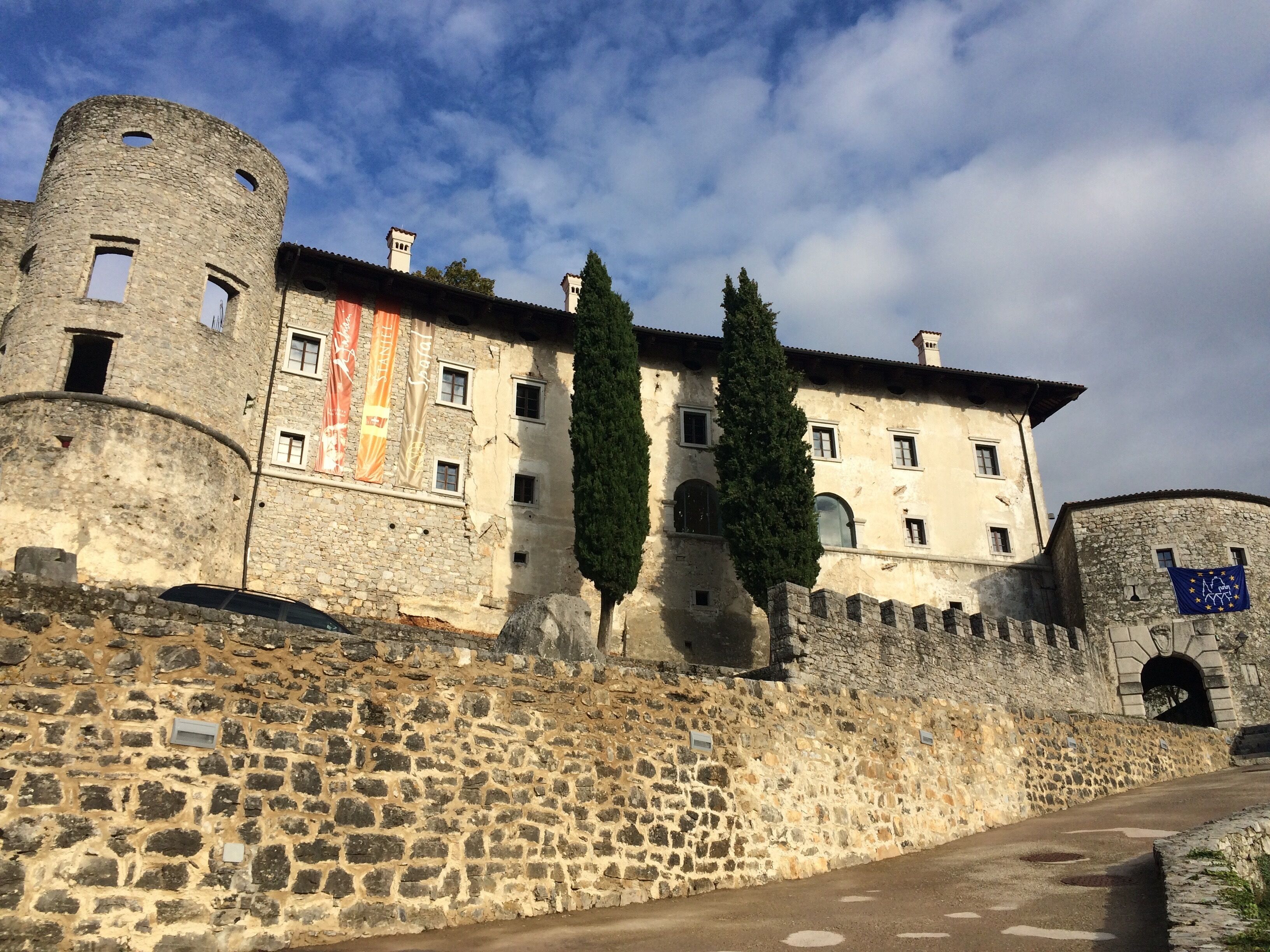 Un bâtiment historique en pierre, doté d’une tour ronde, de fenêtres en arc de cercle et d’un drapeau.