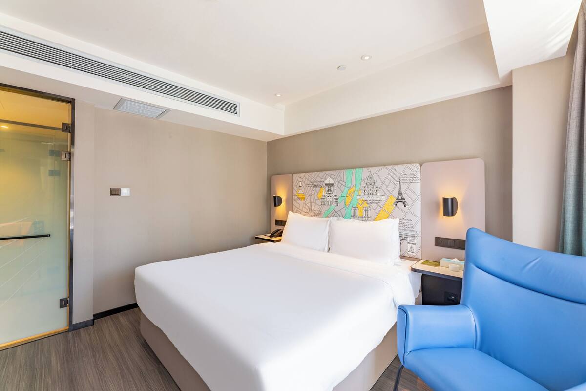 Ein Hotelzimmer mit einem großen Bett, einem blauen Sessel, einer Karte an der Wand und einer Glastür.
