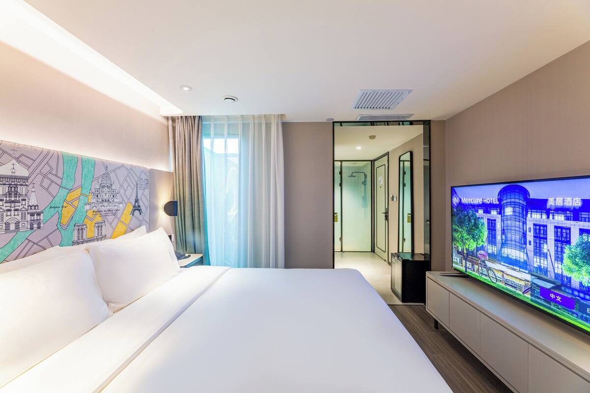 Ein Hotelzimmer mit einem großen Bett, einem Fernseher, einer Karte an der Wand und Blick auf die Stadt durch das Fenster.