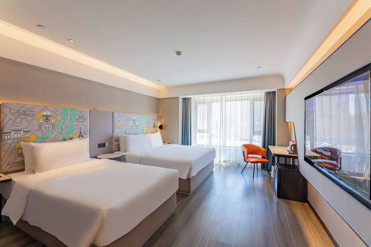 Ein Hotelzimmer mit zwei Betten, einem Schreibtisch, einem Stuhl und einem großen Fenster.