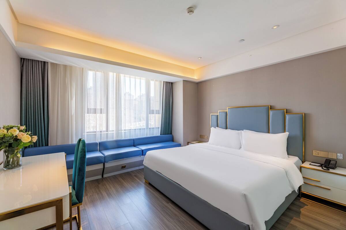 Ein Hotelzimmer mit Bett, Nachttisch, Sofa und einer Vase mit Blumen.