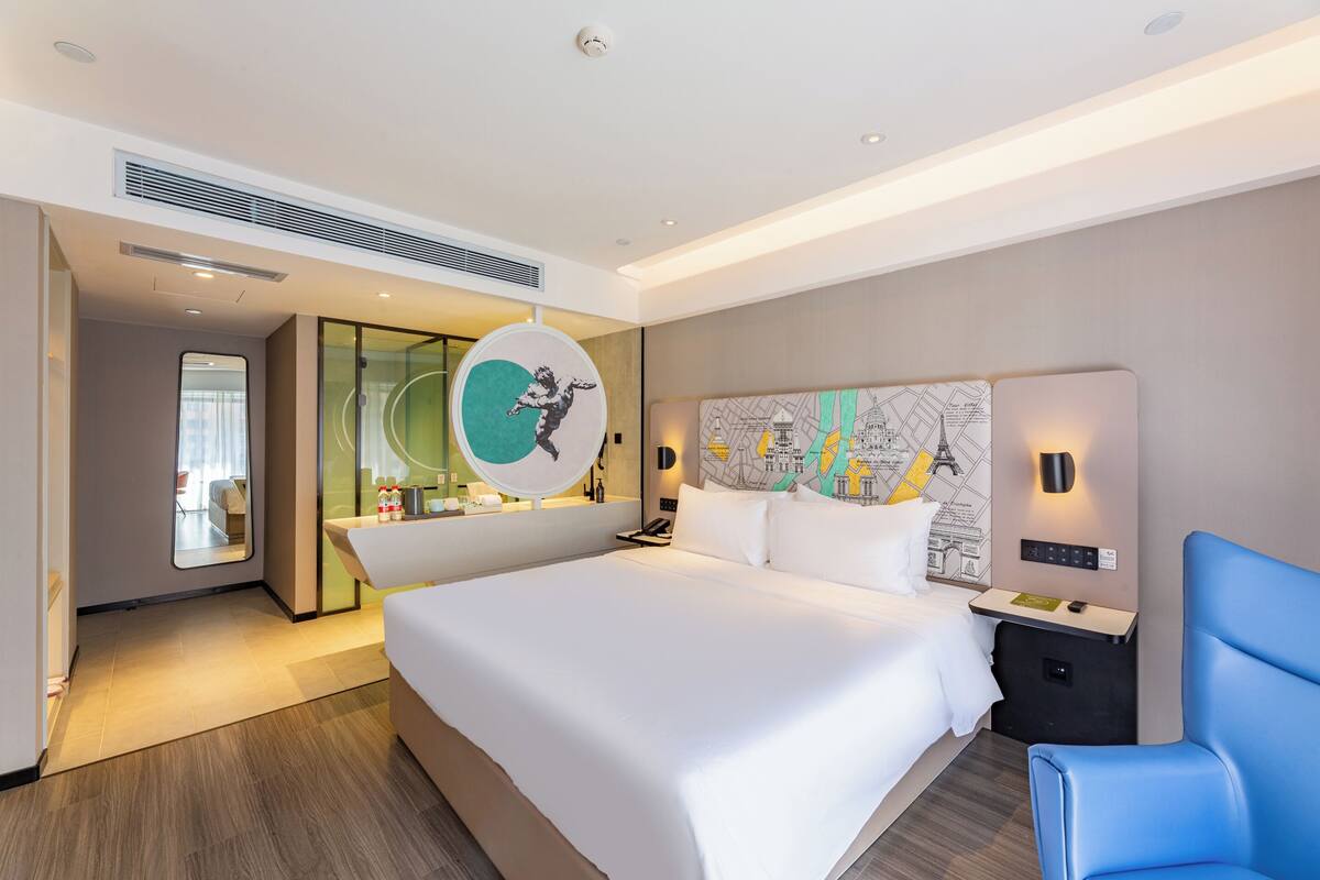 Ein modernes Hotelzimmer mit einem großen Bett, einem blauen Sessel, einer Karte an der Wand und einem Spiegel.