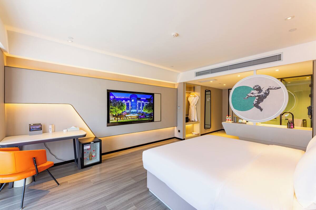 Ein modernes Hotelzimmer mit Bett, Schreibtisch, Sessel, Fernseher und Spiegel.