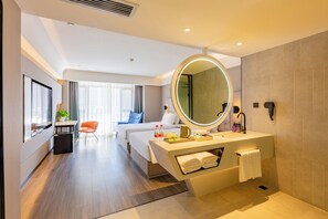A hotel room with a bed, a desk, a chair, a round mirror, a sink, and a window. - Mercure Harbin West Station (Harbin)