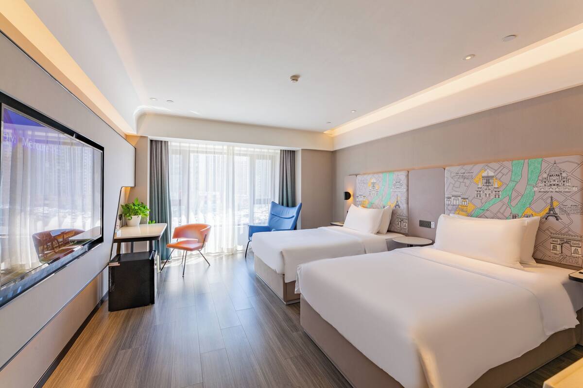 Ein Hotelzimmer mit zwei Betten, einem Schreibtisch, einem Stuhl, einem Fernseher und einem großen Fenster.