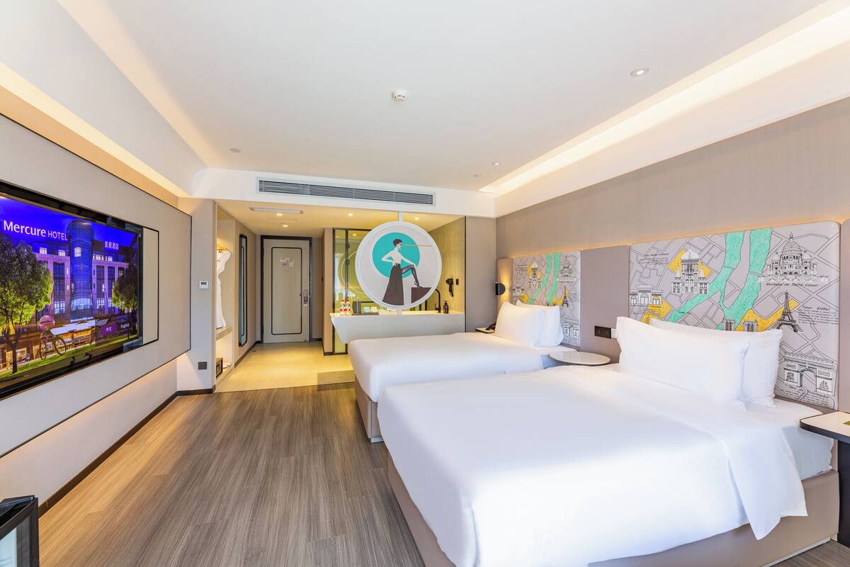 Ein Hotelzimmer mit zwei Betten, einem Fernseher, einer Karte an der Wand und Blick auf das Hotelgebäude.