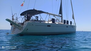 Eine große Segelyacht mit abgedecktem Deck und mehreren Masten, die auf ruhigem, blauem Wasser treibt.