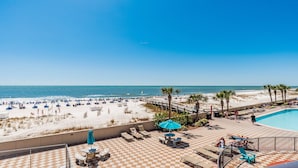A beach resort with a pool, lounge chairs, and a view of the ocean.