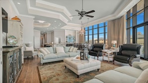 A spacious living room with a large window, a ceiling fan, and a dining area with a chandelier.