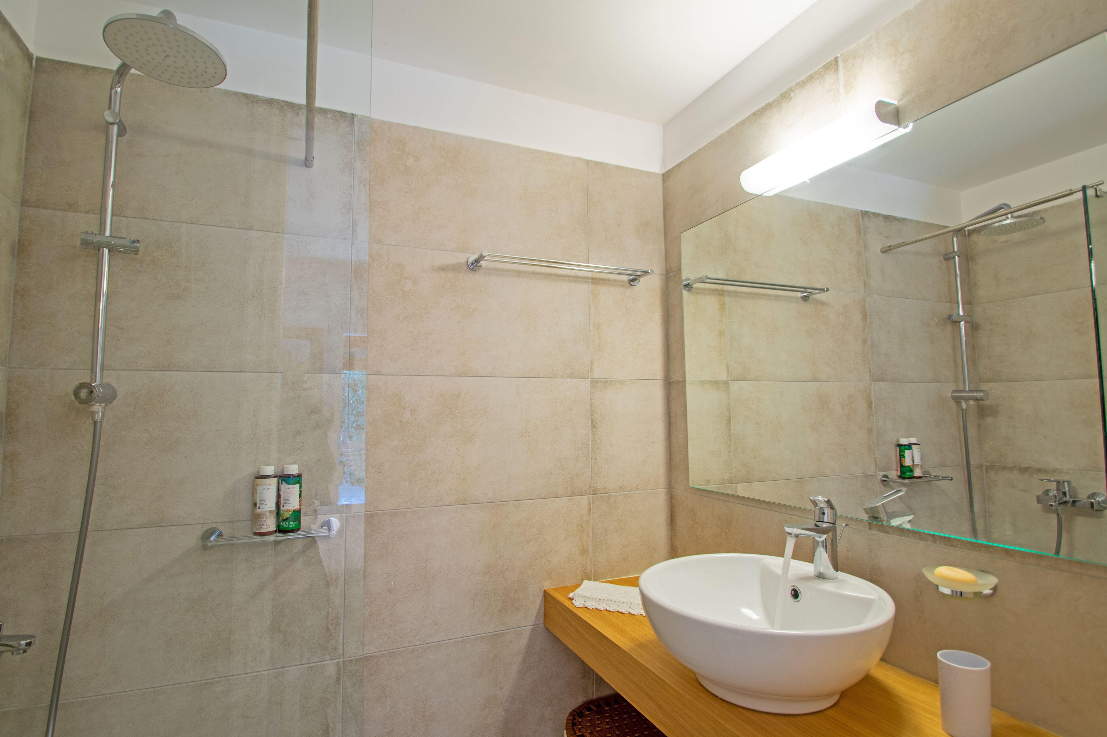 Une salle de bain moderne avec un grand miroir, un lavabo blanc et une douche à parois de verre.