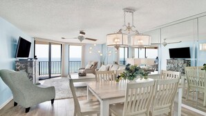 A spacious living room with a large dining table, comfortable seating, and a view of the ocean through large windows. - New to the Rental Market, New Owner, Newly Renovated!!! (Orange Beach)