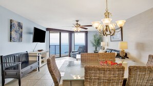 A spacious living room with a balcony, a ceiling fan, a chandelier, and a flat-screen TV. - New to the Rental Market, Newly Owner, Newly Renovated!!! (Orange Beach)