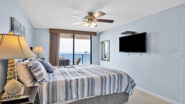 Une chambre d’hôtel avec un lit, un ventilateur de plafond, une télévision et une vue sur la mer.