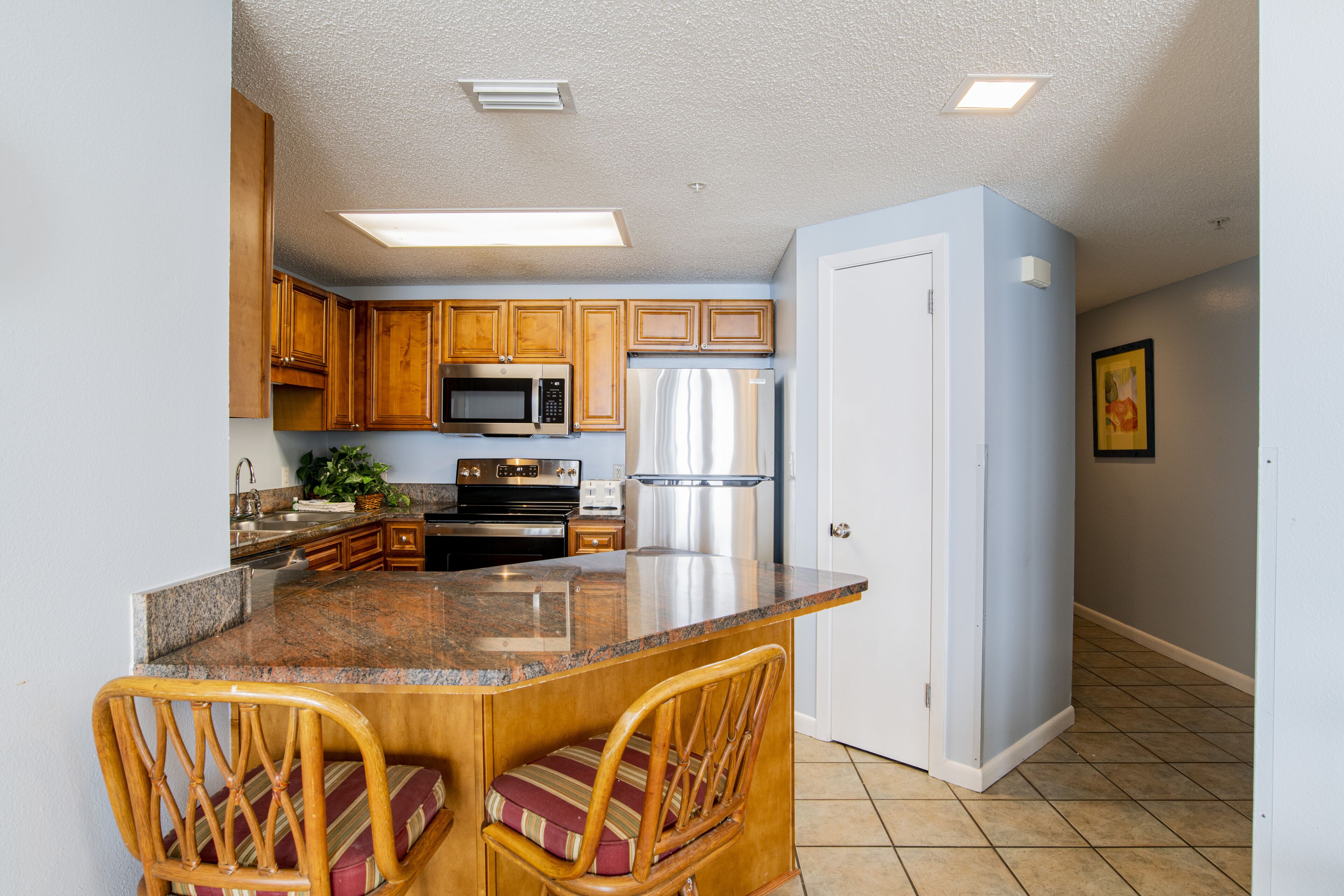 A kitchen with wooden cabinets, stainless steel appliances, a granite countertop, and a built-in island with bar stools.