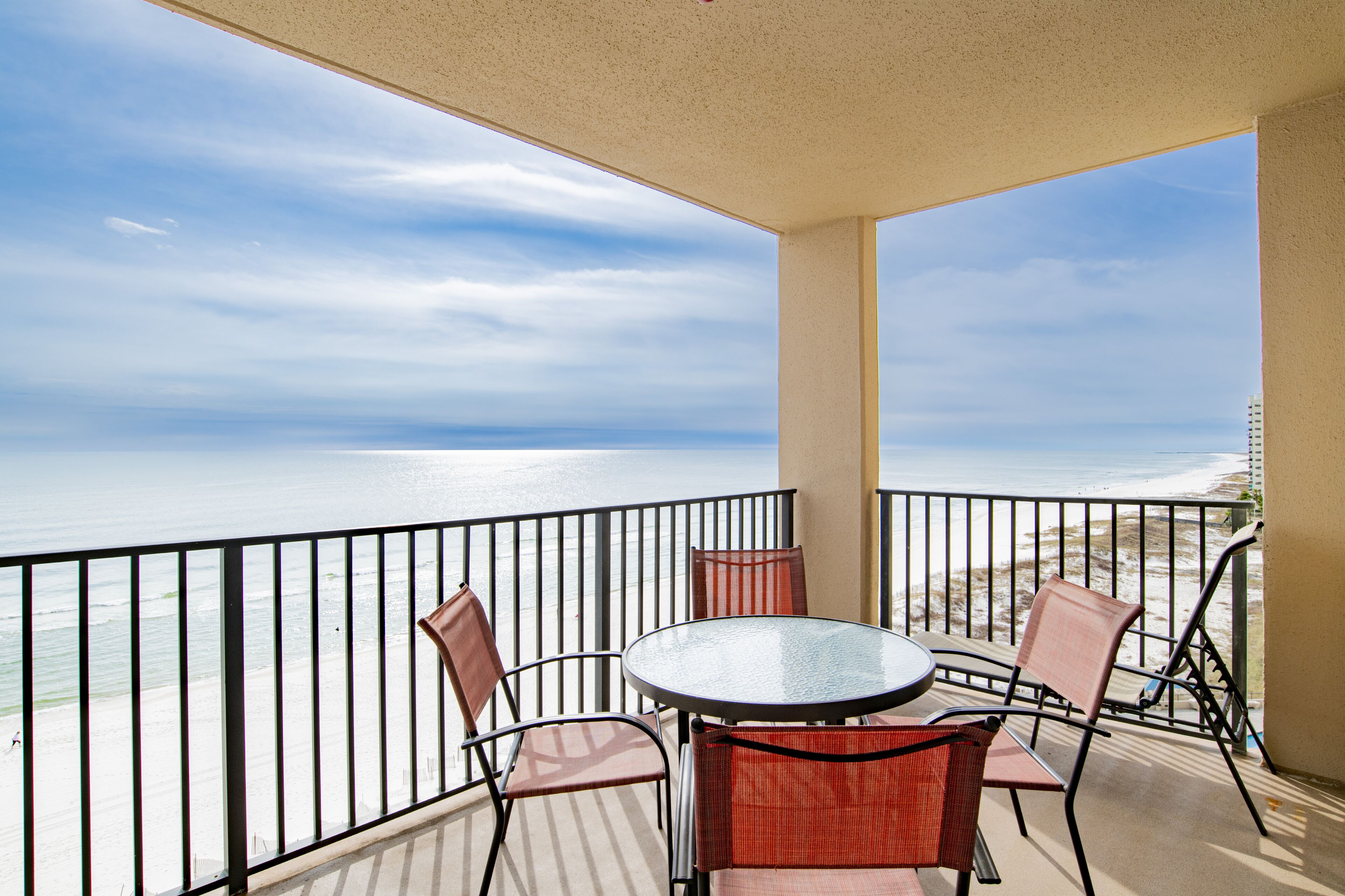 Ein Balkon mit Glastisch und Stühlen, mit Blick auf einen Strand und den Ozean.