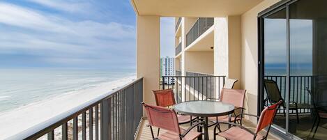 A balcony with a table and chairs overlooking a beach.