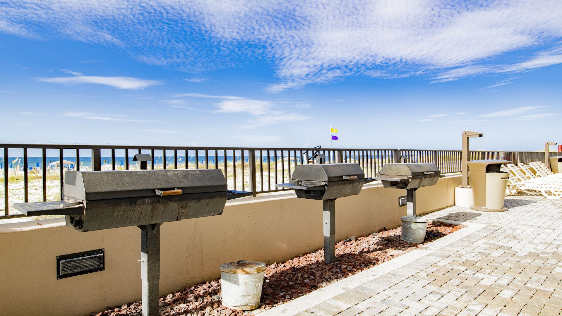 A beachside walkway with barbecue grills and a trash can.