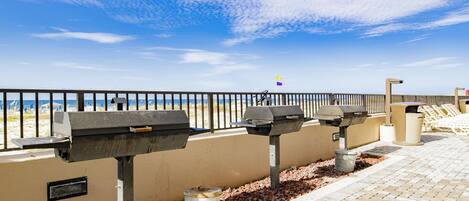 A beachside walkway with barbecue grills and a trash can.