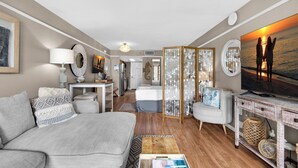 A cozy living room with a sofa, a coffee table, and a TV. There is a decorative screen and a painting on the wall. - 🌊View~FREE BeachService~Steps2Beach~Heated Pool~1BR Islander Beach Resort 305🌅 (Fort Walton Beach)