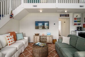 Uma sala de estar com escada, um quadro, uma cafeteira e uma estante de livros.