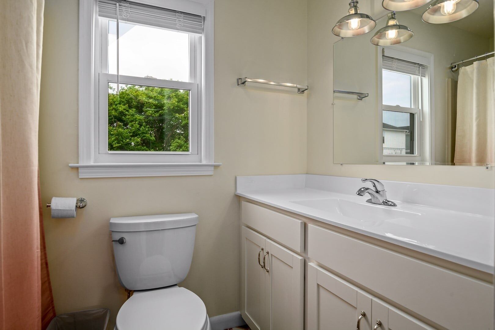 Une salle de bain avec des toilettes, un lavabo, un miroir et une fenêtre.
