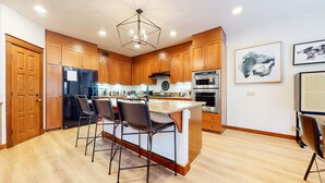 A modern kitchen with wooden cabinets, a black refrigerator, a stainless steel oven, and a bar area with stools. - Timbers 6 Updated and Pet-Friendly, Private Jacuzzi, Private Garage by RedAwning (Mammoth Lakes)