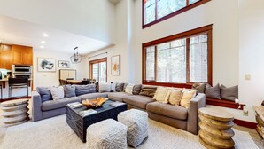 A spacious living room with a sectional sofa, a coffee table, and a dining area with a kitchen in the background. - Timbers 6 Updated and Pet-Friendly, Private Jacuzzi, Private Garage by RedAwning (Mammoth Lakes)