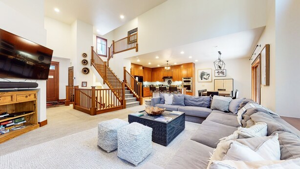 A spacious living room with a large sofa, a coffee table, and a TV. There is a staircase leading to an upper level. - Timbers 6 Updated and Pet-Friendly, Private Jacuzzi, Private Garage by RedAwning (Mammoth Lakes)