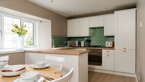 A modern kitchen with white cabinetry, a green backsplash, and a wooden island with a dining table and chairs.