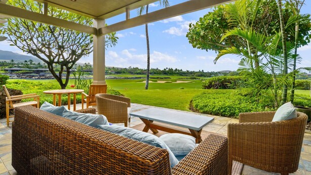 A covered outdoor seating area with wicker furniture, a table, and chairs, overlooking a golf course.