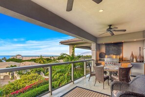 Ein Balkon mit Blick auf ein Resort und den Ozean, einem Deckenventilator und einer Küchenzeile mit Grill.