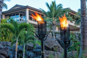 A resort with two lit torches, a waterfall, and a modern building with balconies.