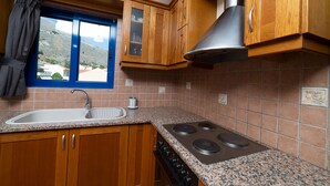 A kitchen with wooden cabinets, a granite countertop, a stainless steel range hood, and a window with a view of the outdoors.