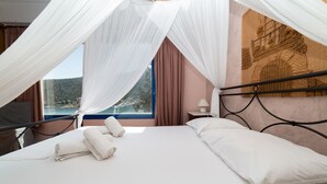 A bed with white linens, a canopy, and a view of a coastal landscape.