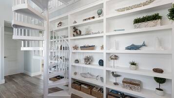 Un escalier en colimaçon blanc mène à une étagère à plusieurs niveaux, où sont disposés divers objets décoratifs et des paniers.