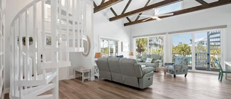 A spacious living area with a spiral staircase, a grey sofa, and a balcony with large windows.