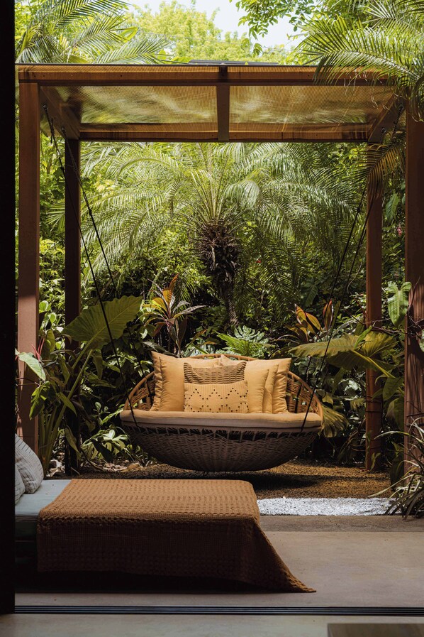 A hammock chair under a wooden pergola with lush tropical foliage in the background.