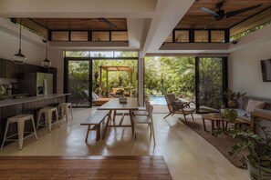 A modern kitchen with a bar area, a dining table with benches, and a large sliding glass door leading to a pool and garden.
