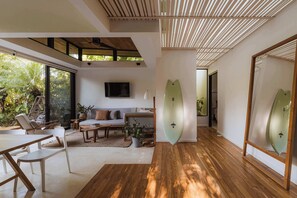 A modern interior with a wooden floor, a sofa, a dining table, and a surfboard on display.